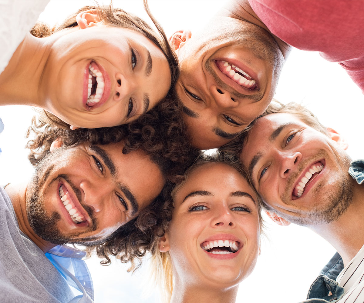 The image shows a group of six young adults with smiles on their faces, posing together for a photo with their heads overlapping in the center, creating a sense of unity.